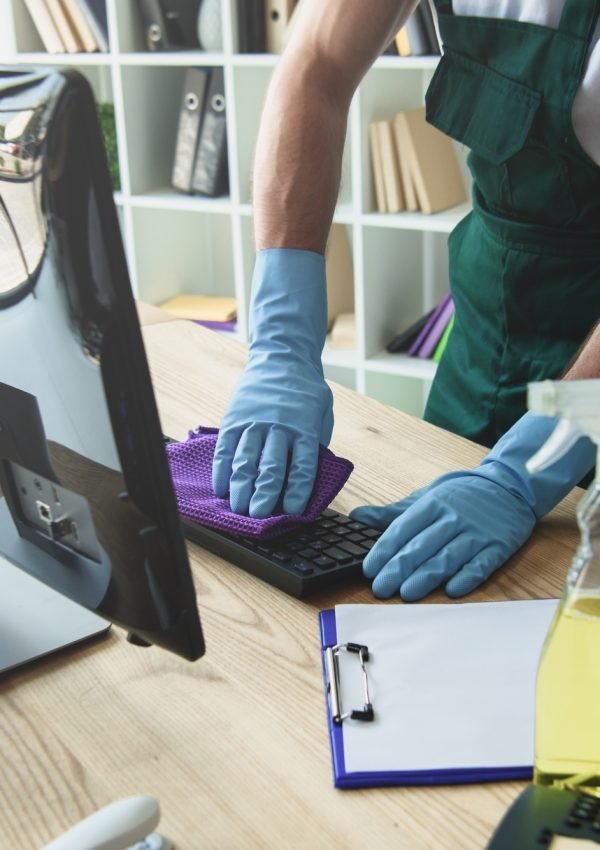 cropped shot of professional cleaner in rubber gloves cleaning computer keyboard in office